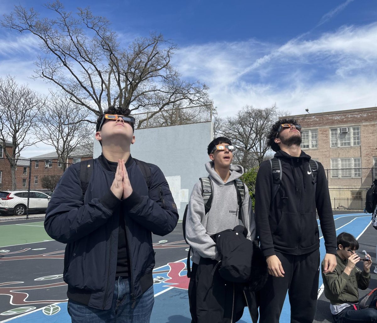 Left to right: Alexander Kaziyev, Dylan Kaziyev, Enian Qosja in the schoolyard looking up at the solar eclipse. Christian Kelly sitting, putting on his solar viewers.